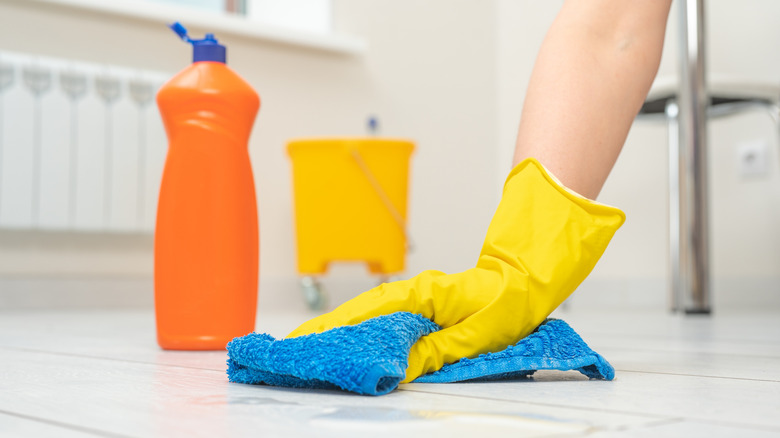 Gloved hand wiping floor with soft cloth and cleaning solution