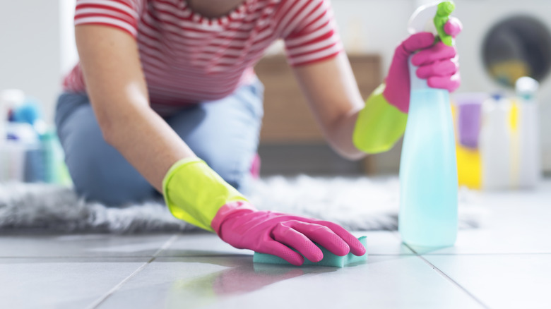 Woman cleans floor with spray and sponge.