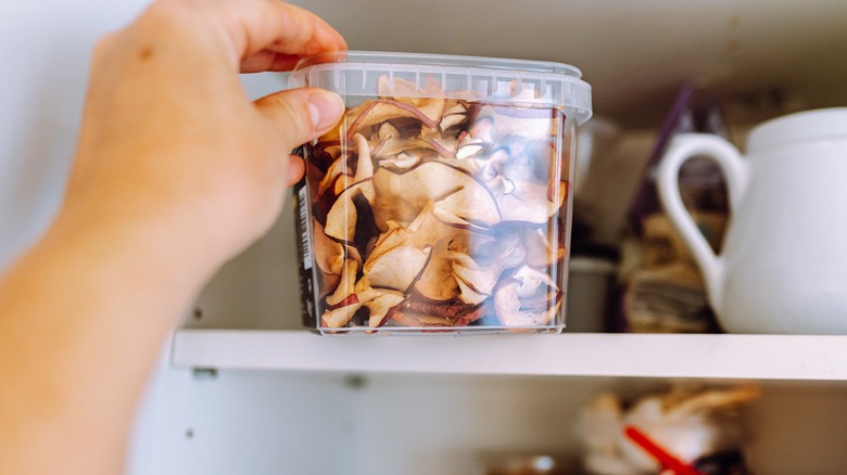 A person's hand holding a clear container of dried apples on a shelf