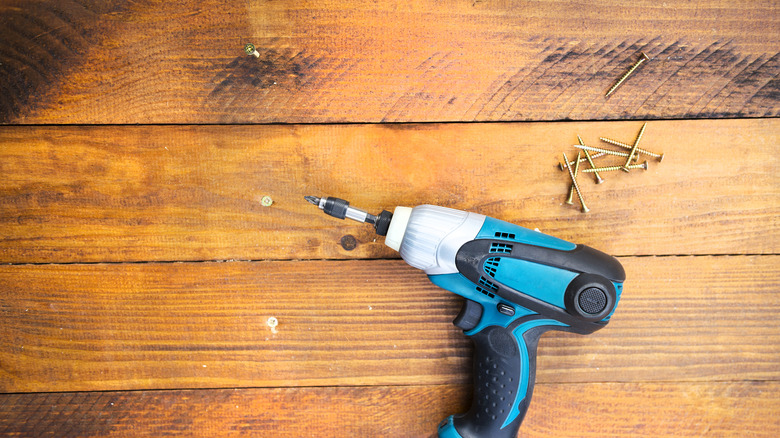 Electric screwdriver and screws on wooden floor