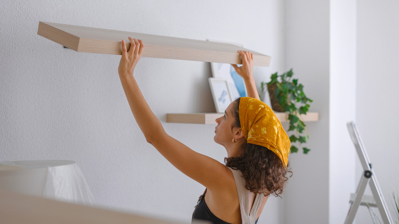 Woman putting up a pair of floating shelves in her home