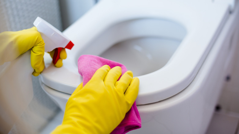 A person wearing yellow gloves cleans a toilet