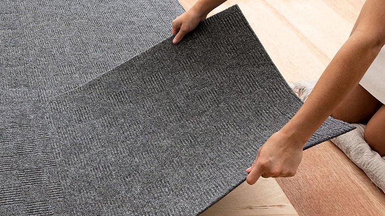 woman placing large gray low pile carpet tile