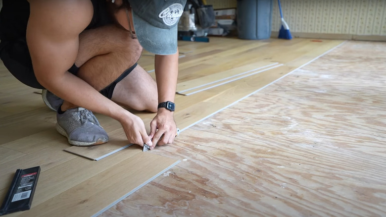 man trimming light engineered hardwood floorboards over subfloor