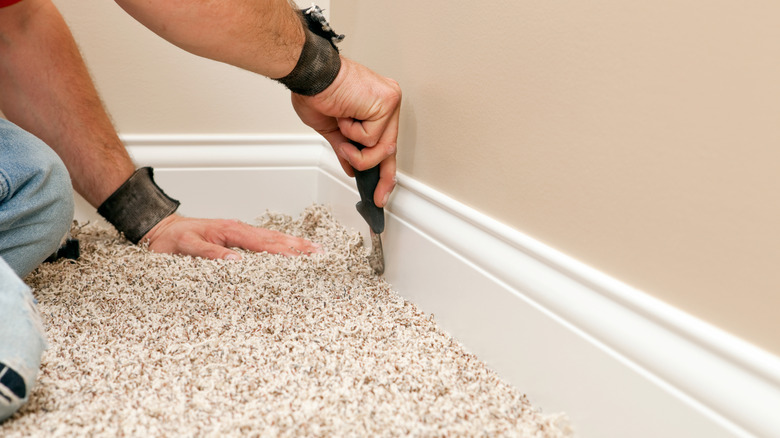 man trimming beige stretch-in carpet with utility knife