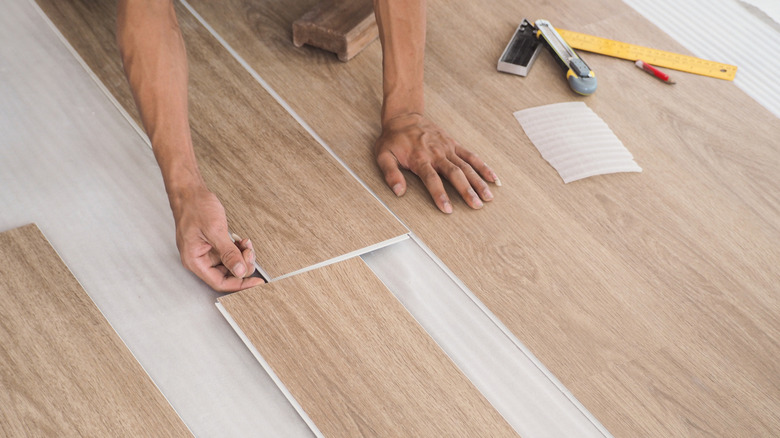 person laying LVP flooring with ruler, pencil, and utility knife