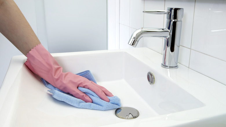 Gloved hand cleans bathroom sink