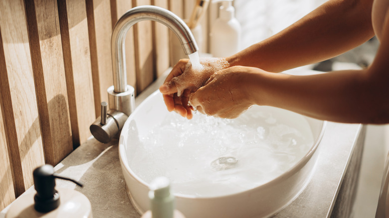 person washing hand in bathroom sink