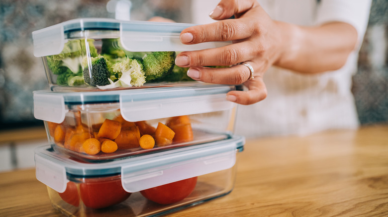 Person stacking glass food containers with vegetables