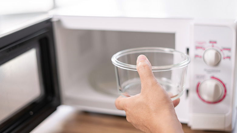 A hand holding a glass container in front of microwave