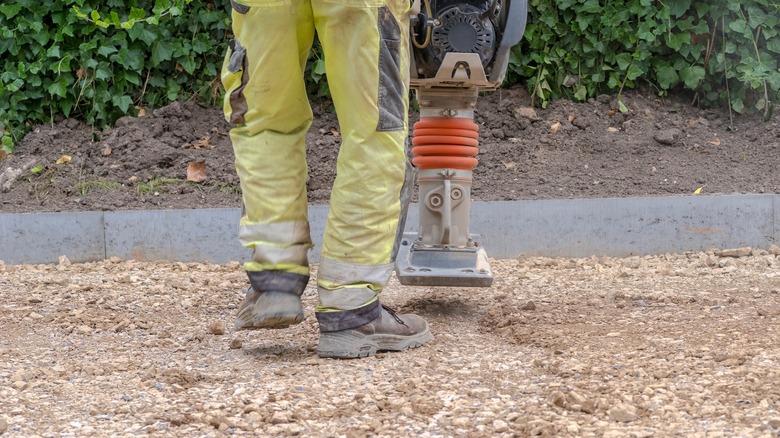 A person tamps a gravel base layer