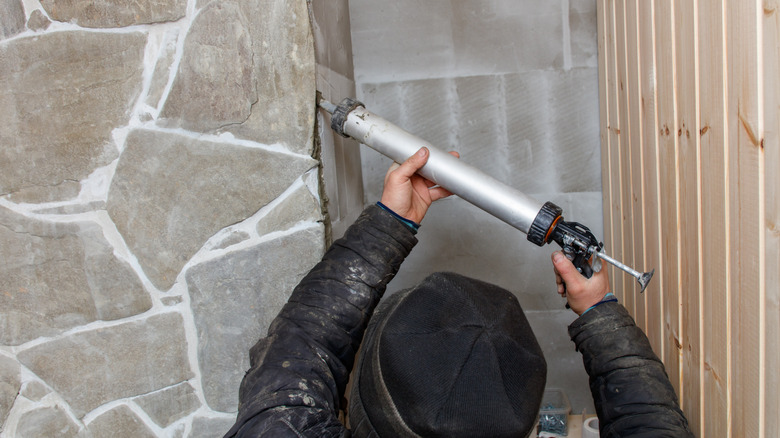 A man with a black hat and black jacket caulking a wall