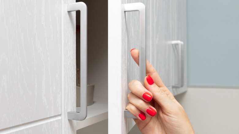 Woman opening overhead cabinet door with silver handle