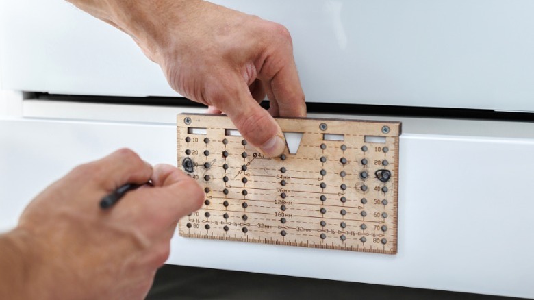 Man setting cabinet handle hole marks with template over white drawer