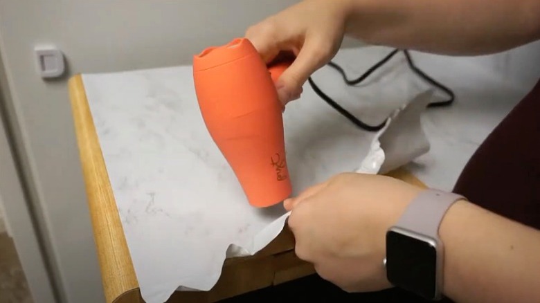 Woman removing contact paper from a narrow kitchen counter using an orange hairdryer.