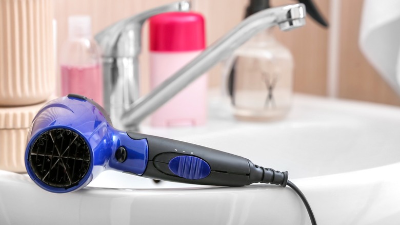 Blue hair dryer sitting on the edge of a bathroom sink.