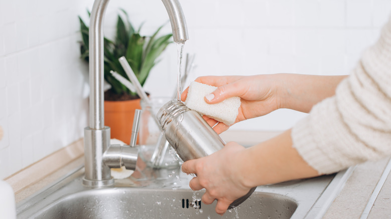 person washing reusable water bottle