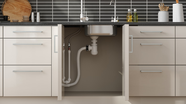 The underside of a kitchen sink between two white cabinets.