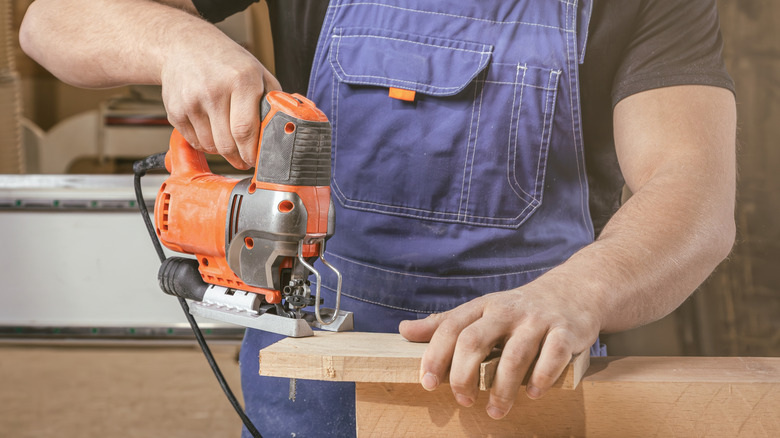 A man uses a jigsaw to cut a piece of wood.