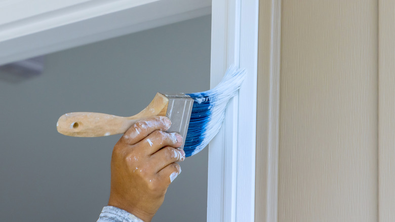 Person applying white paint to door trim