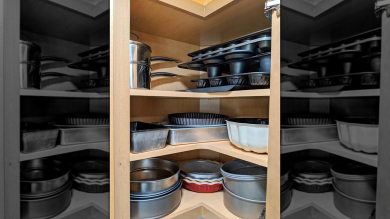 Three corner shelves in a cabinet hold a variety of pots, pans, and baking dishes