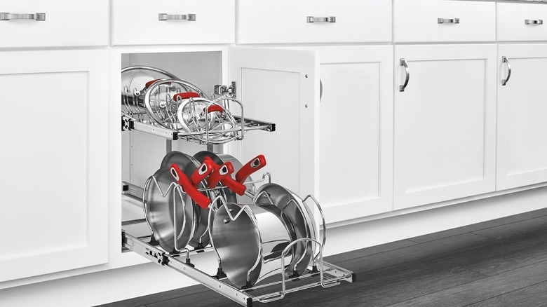 A row of white cabinets are closed save one which reveals the Rev-A-Shelf pots and pan organizer shelving unit, filled with pots, pans, and lids