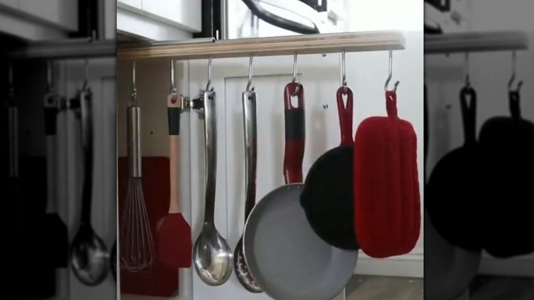 A pullout rack is extended from a cabinet and has several kitchen tools hanging from it on hooks