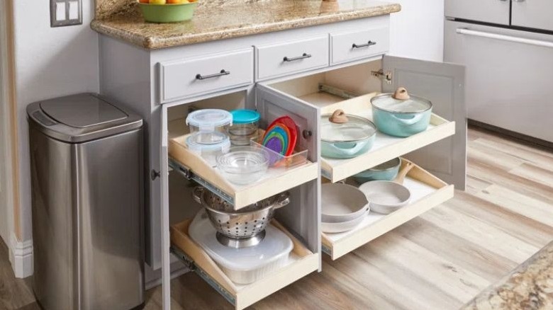 Open white kitchen cabinets reveal a pullout tray drawer filled with stainless steel pots