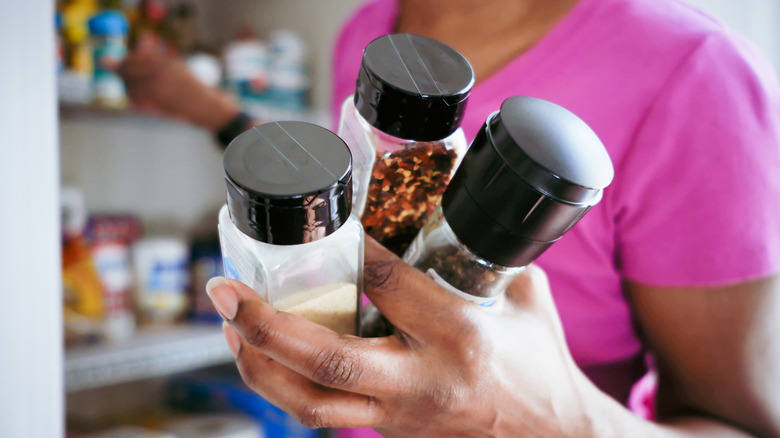 Person holding spice jars in front of open pantry