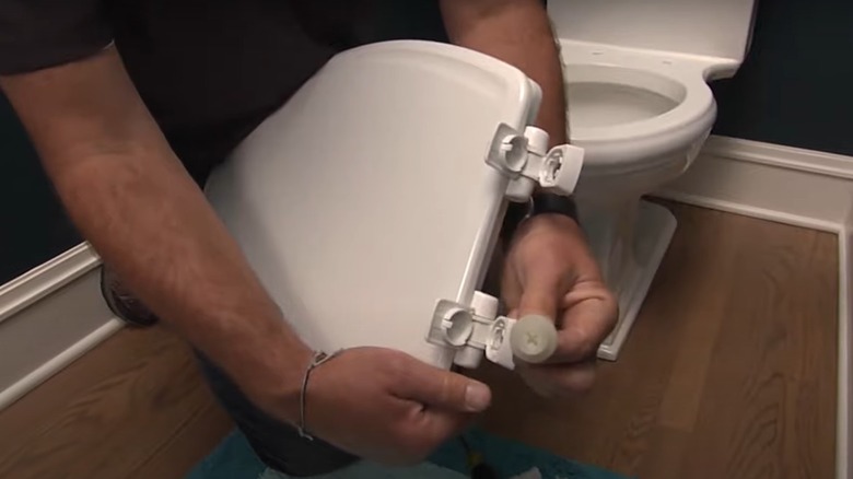 man's hand holding new elongated toilet seat about to install it on toilet