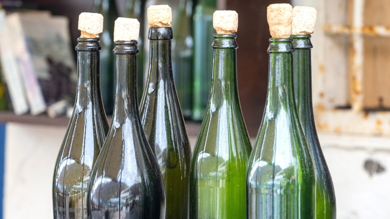 six empty green wine bottles with cork stoppers