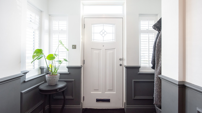 A neat entryway with a plant in the window and coat hanging to the side