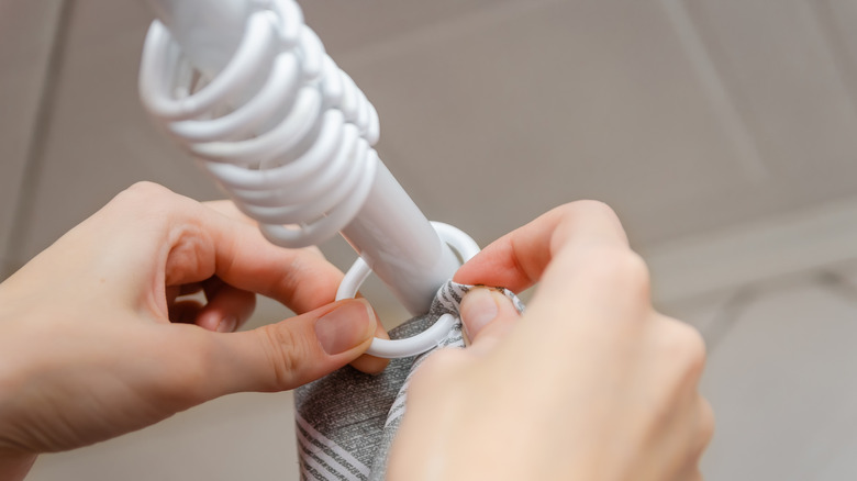 Person hanging shower curtain onto rings