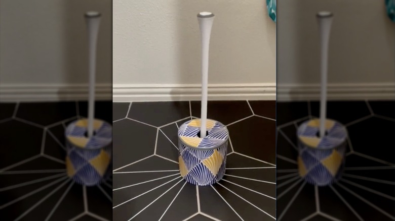 Decorative coffee can covered with blue and yellow striped wallpaper holding a plunger