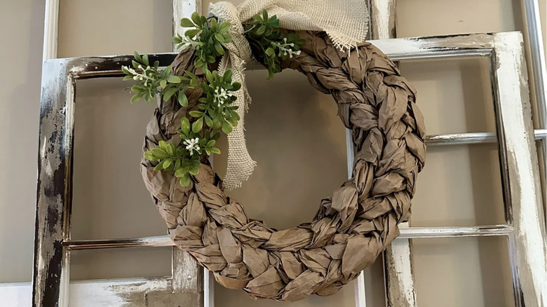 A wreath made of braided packing paper is hanging from a repurposed window frame.