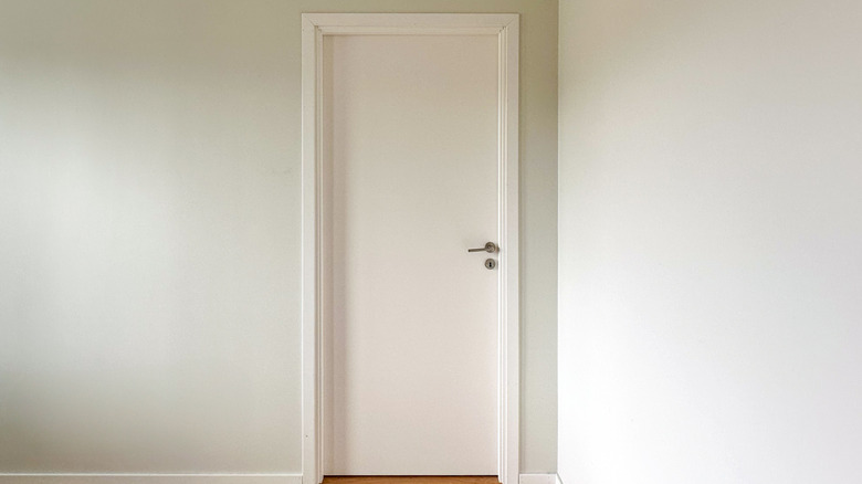 A plain white door in a sparse white room