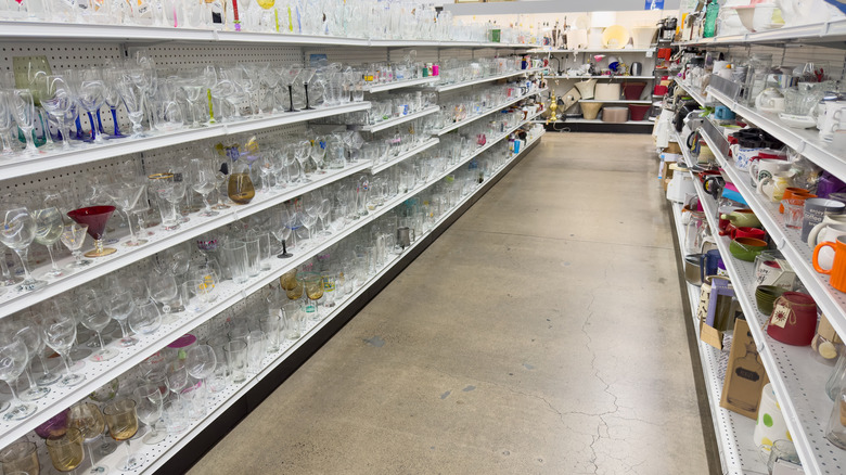 A thrift store glassware aisle has shelves on both sides.