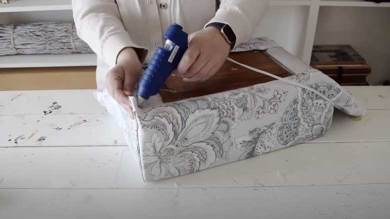 Person adhering fabric to foam with a glue gun