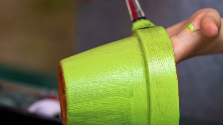 Person painting terra cotta pot green with narrow brush