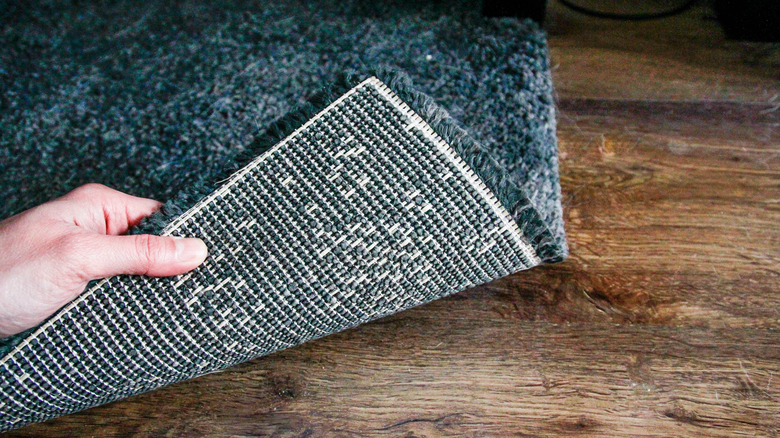 A hand rolls up blue rug from wood floor