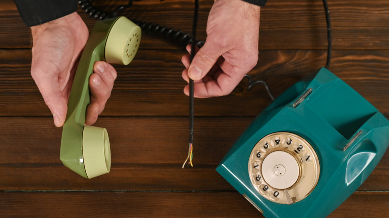 A man holds a rotary phone with wires coming out of it