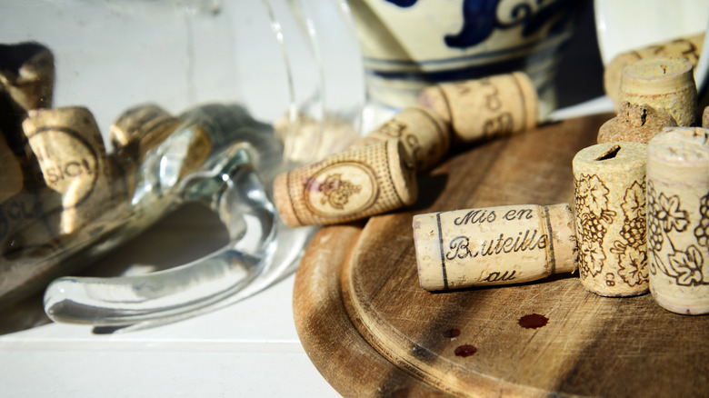 A pile of assorted wine corks sit on a wooden trivet