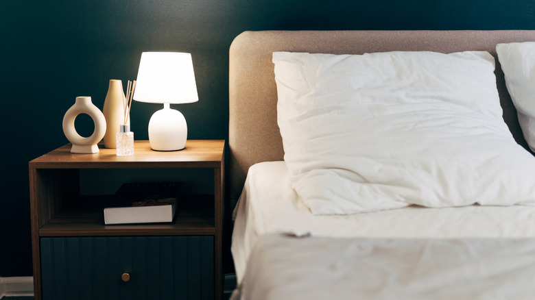 Cream colored fabric headboard in green bedroom with white lamp