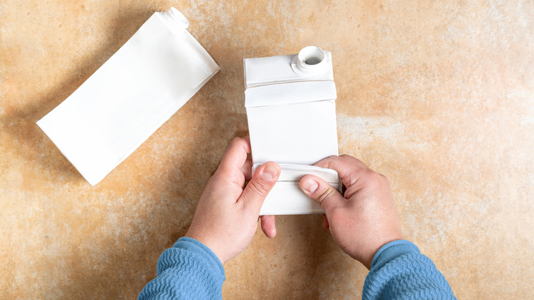 A person folds an empty milk carton