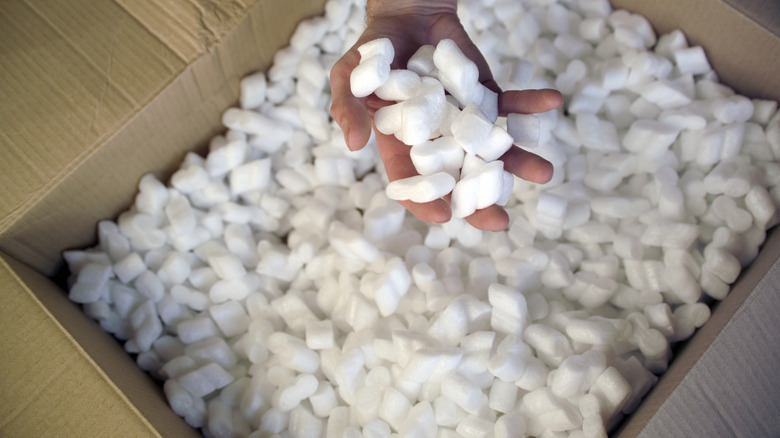 Open box full of packing peanuts, with hand carrying peanuts in foreground