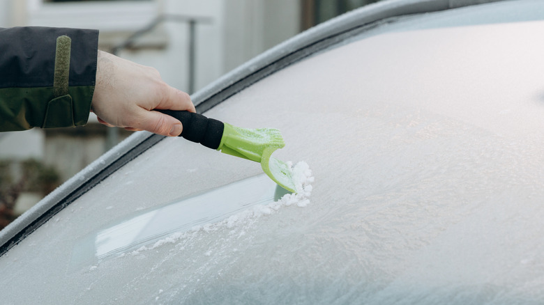 A hand using an ice scraper to deice a windshield