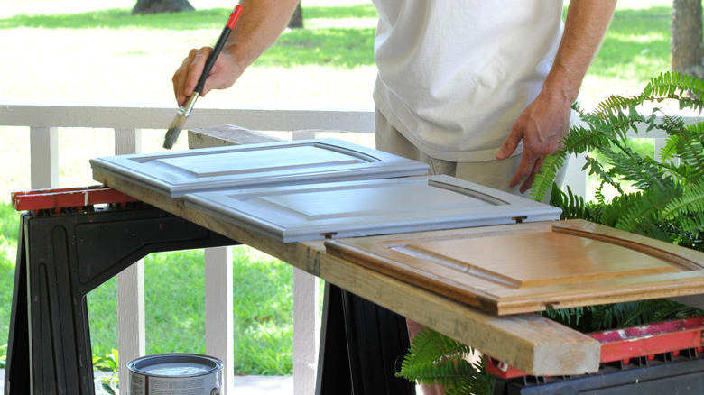 A man painting a cabinet door on a sawhorse outside