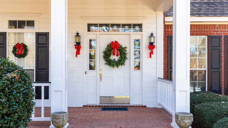 Photo of exterior of a home decorated for Christmas, a green wreath with a red bow adorns the door and window