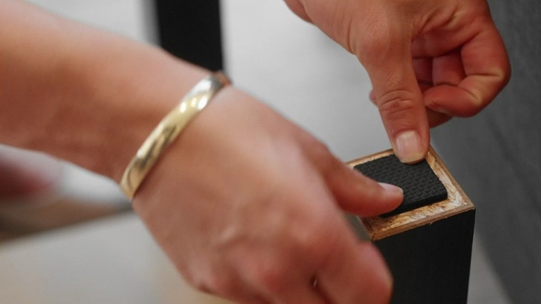 Woman attaching a square rubber furniture slide onto the bottom of a furniture leg