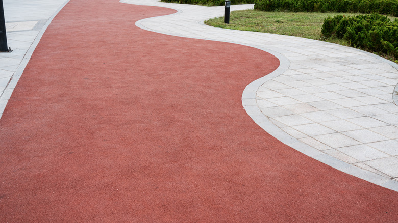 Red Rubber Stone beside paved walkway with lampposts and greenery in the background